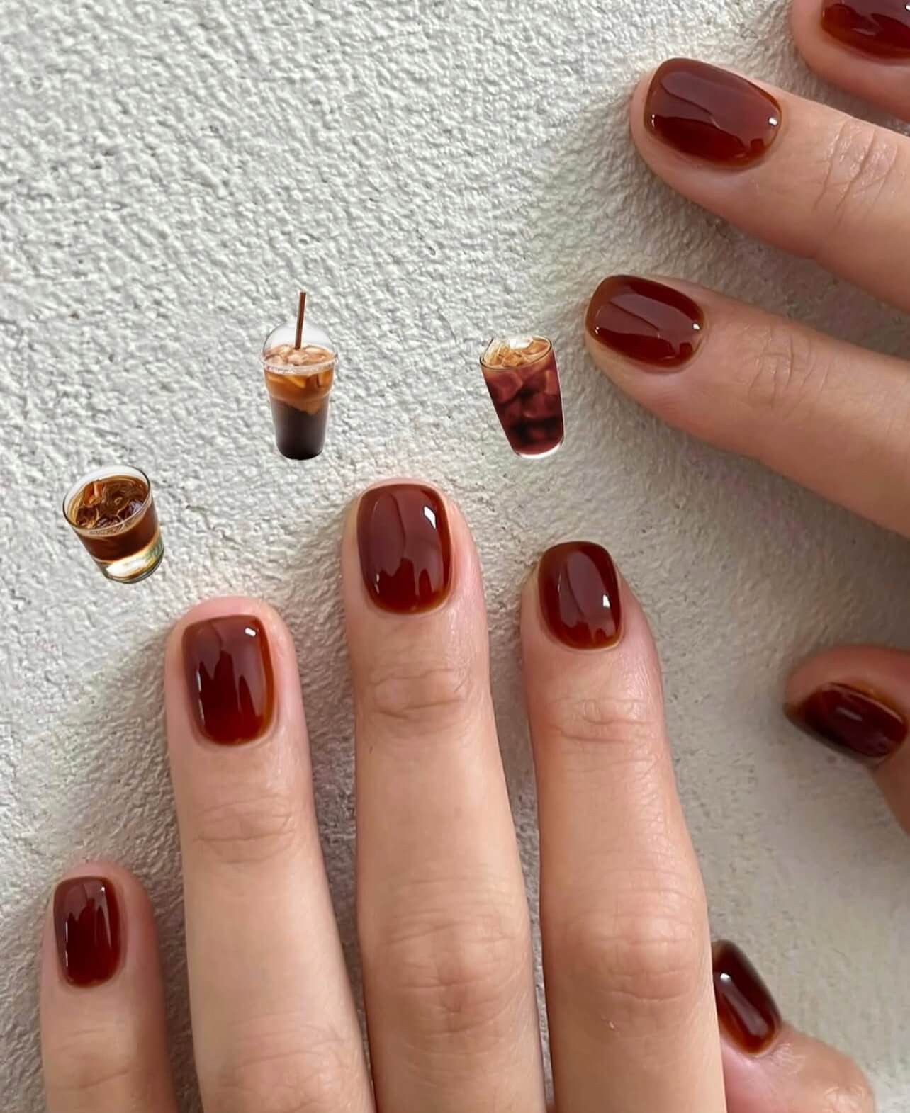 Nails painted Shellac with a dark red color matching miniature coffee cups on a textured surface.